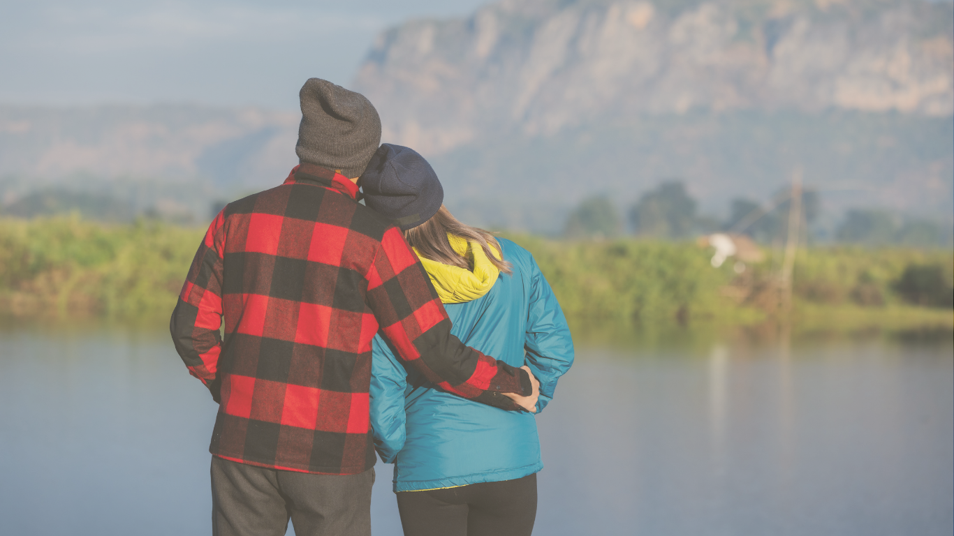 A couple dressed warmly and embracing outside their RV, enjoying full-time RV adventures in scenic surroundings.